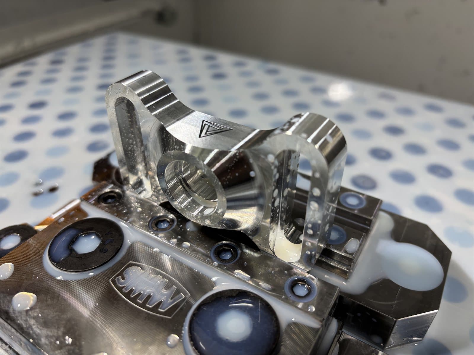 A precision-machined aluminum part with a mirror finish, engraved with the Cambian mark